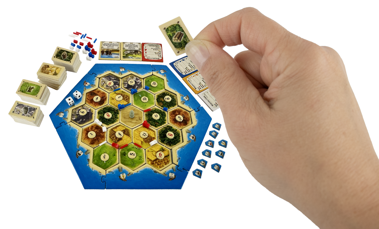 Hand holding a mini resource card over a compact, travel-sized Catan board game set up for play.