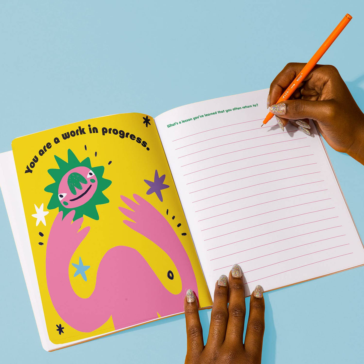 Person writing in the colorful Gentle Reminders Guided Journal open to an inspirational illustrated page and lined prompts page