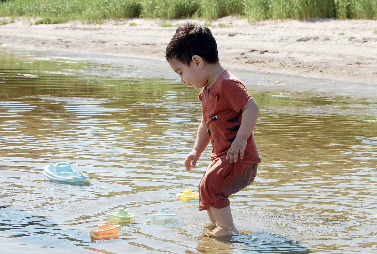 Child playing with pastel-colored Re:line Tub Boat toys in shallow beach water on a sunny day.