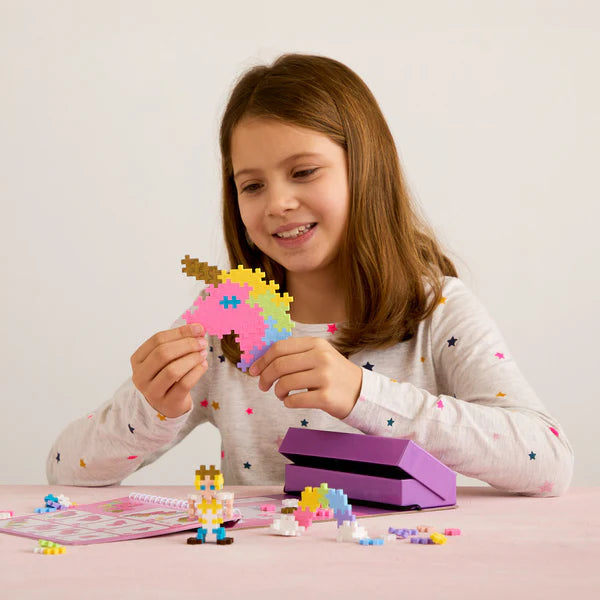 Girl playing with a unicorn creation from the Plus Plus Activity Pad | Fairy Tale with colorful building pieces and storage box.