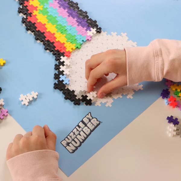 Hands assembling a colorful Plus Plus Puzzle by Number | Rainbow on a blue pattern board.