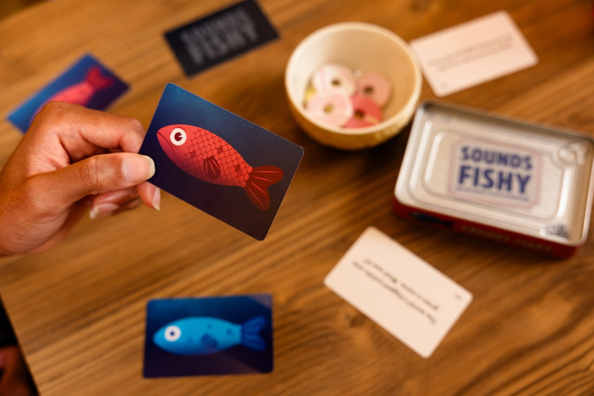 Sounds Fishy Travel Tin with colorful fish cards and game pieces on a wooden table