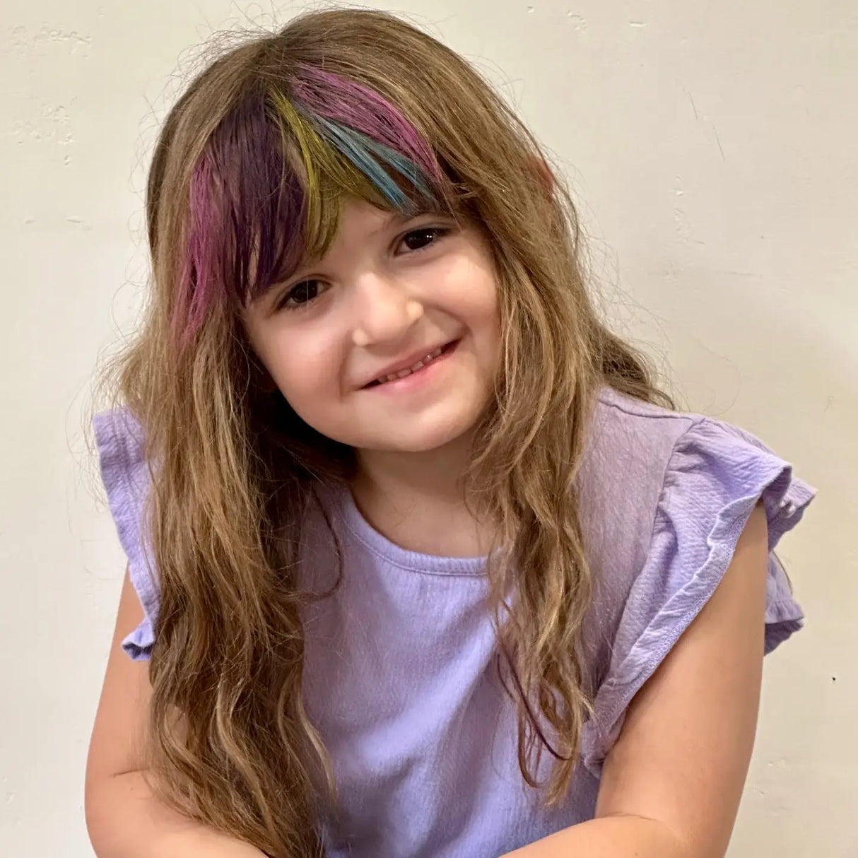 Smiling young girl with colorful streaks in hair using Hair Flair Color Gel Sticks for temporary bright hair color.