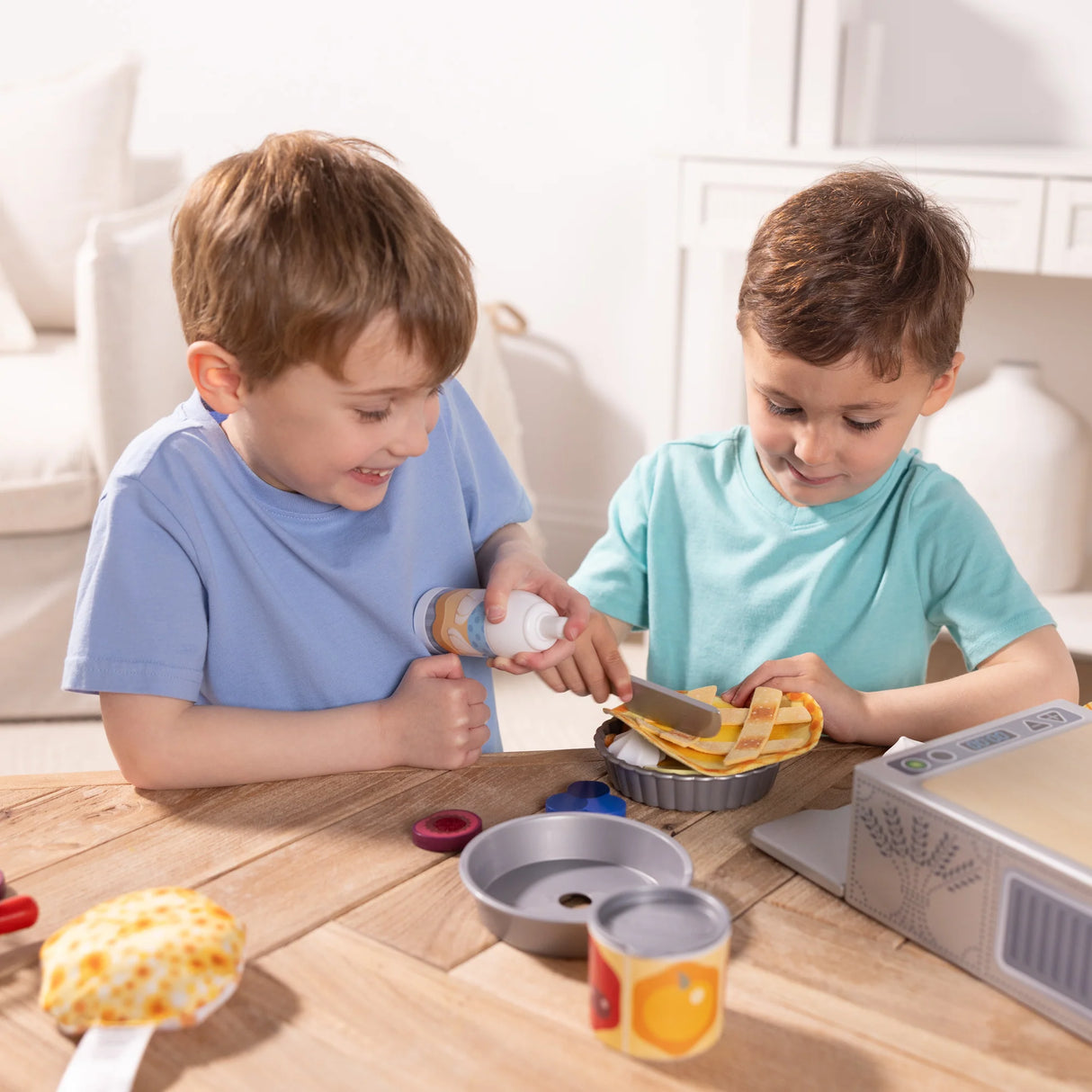Two young boys playing with a Make Bake Pies Play Set crafting fabric pies at a wooden table in a bright room