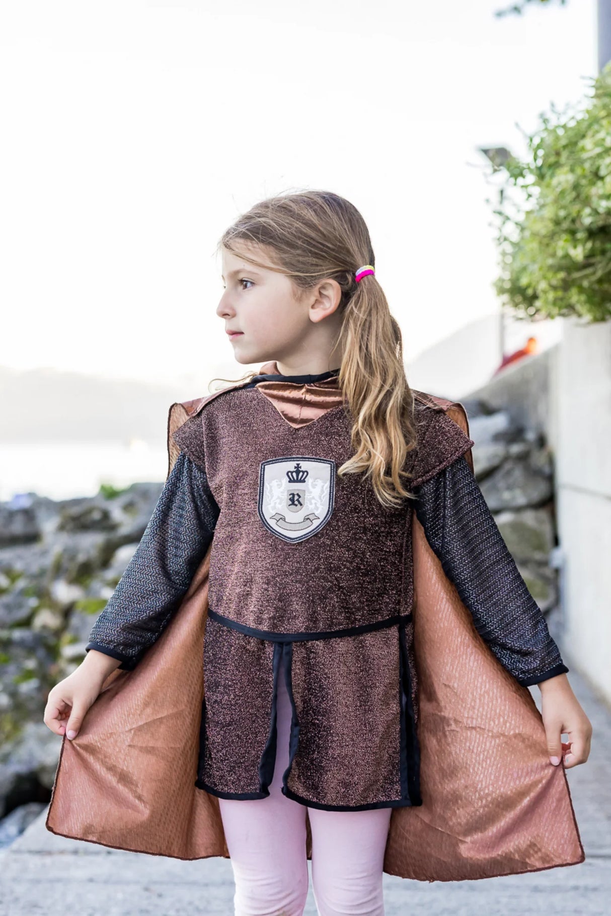 Child wearing Brilliant Copper Knight Tunic with Cape in sparkly brown fabric and iridescent copper cape outdoors.