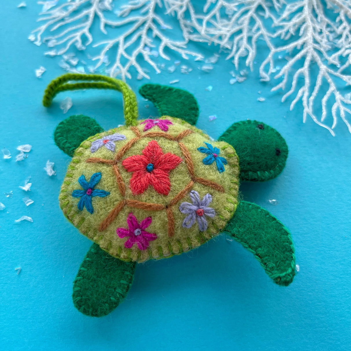 Green felt sea turtle ornament with colorful floral embroidery on its shell against a blue background