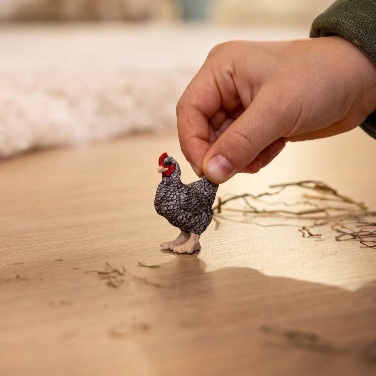 Hand holding a small, detailed Plymouth Rock Chicken figurine with black and white striped feathers on a wooden surface.