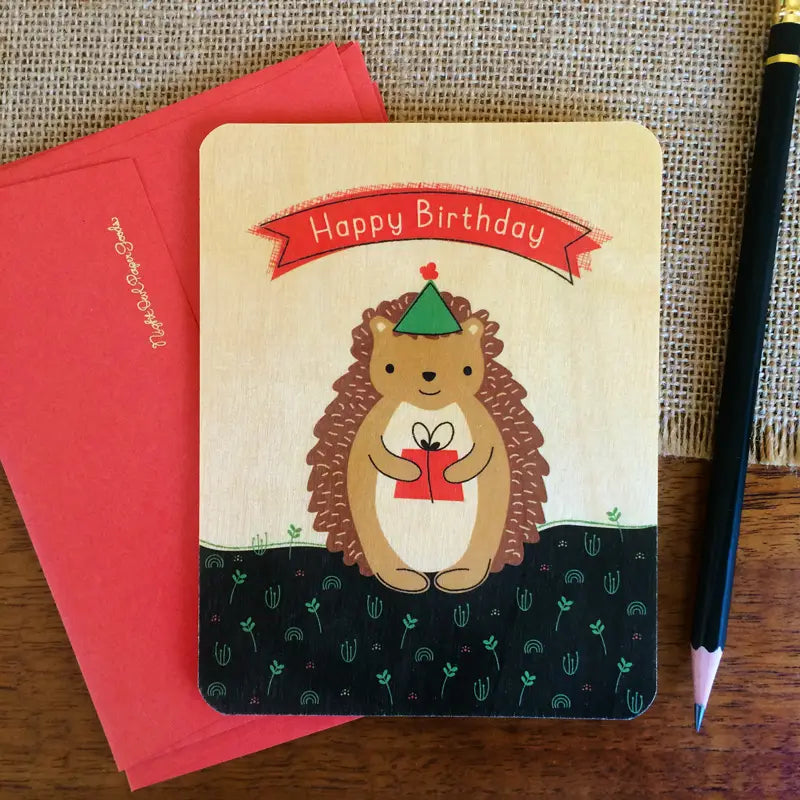 Hedgehog Gift Birthday Wood Card with happy hedgehog holding a gift on sustainable birch wood, includes red envelope.