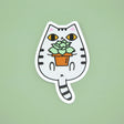 Gray Tabby Cat and Plant Sticker featuring a cute white tabby cat holding a potted green succulent plant on a green background.
