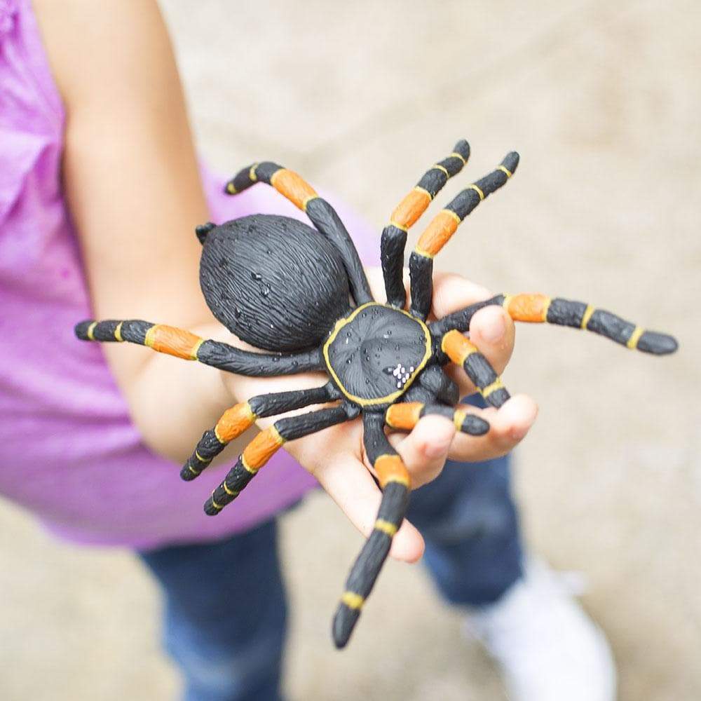 Child holding a realistic Orange-Kneed Tarantula model with black and orange legs in hand close-up view.