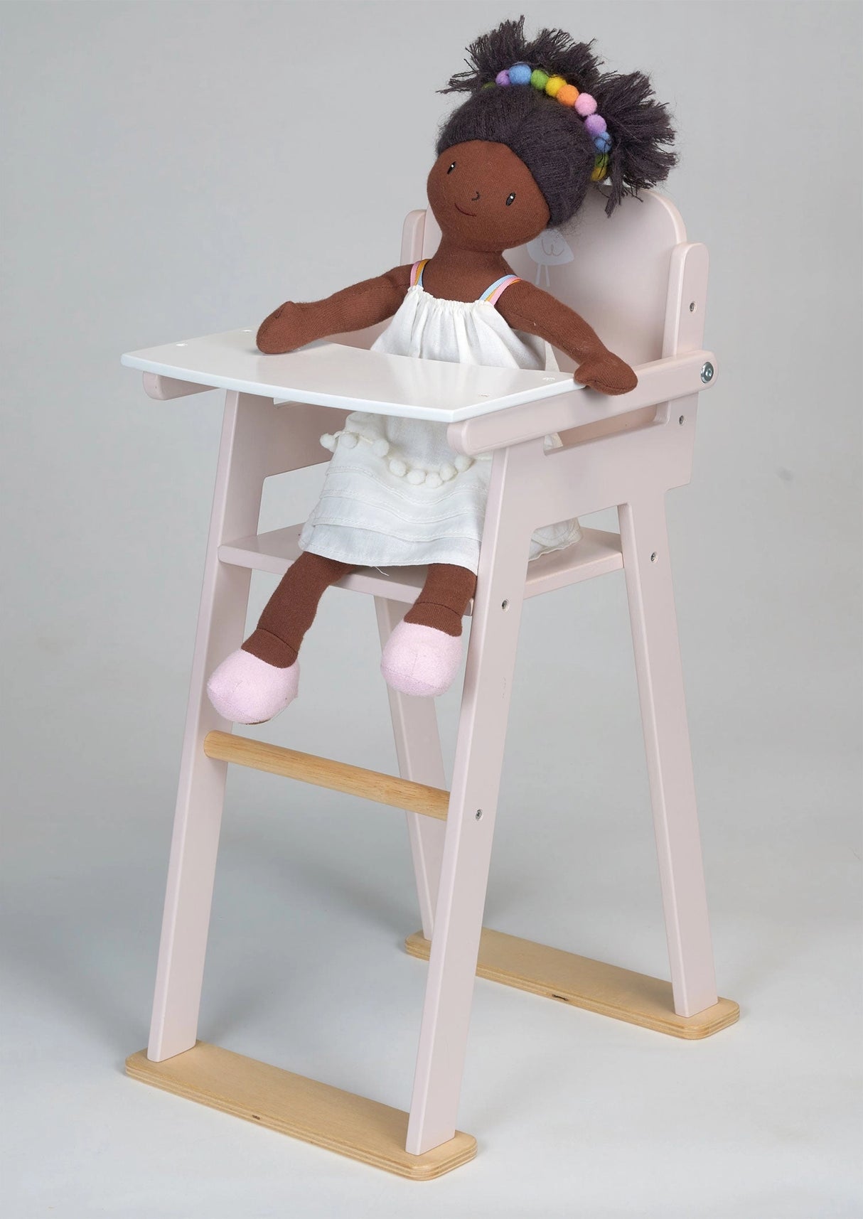 Wooden baby doll high chair with a white tray holding a doll wearing a white dress and pink shoes