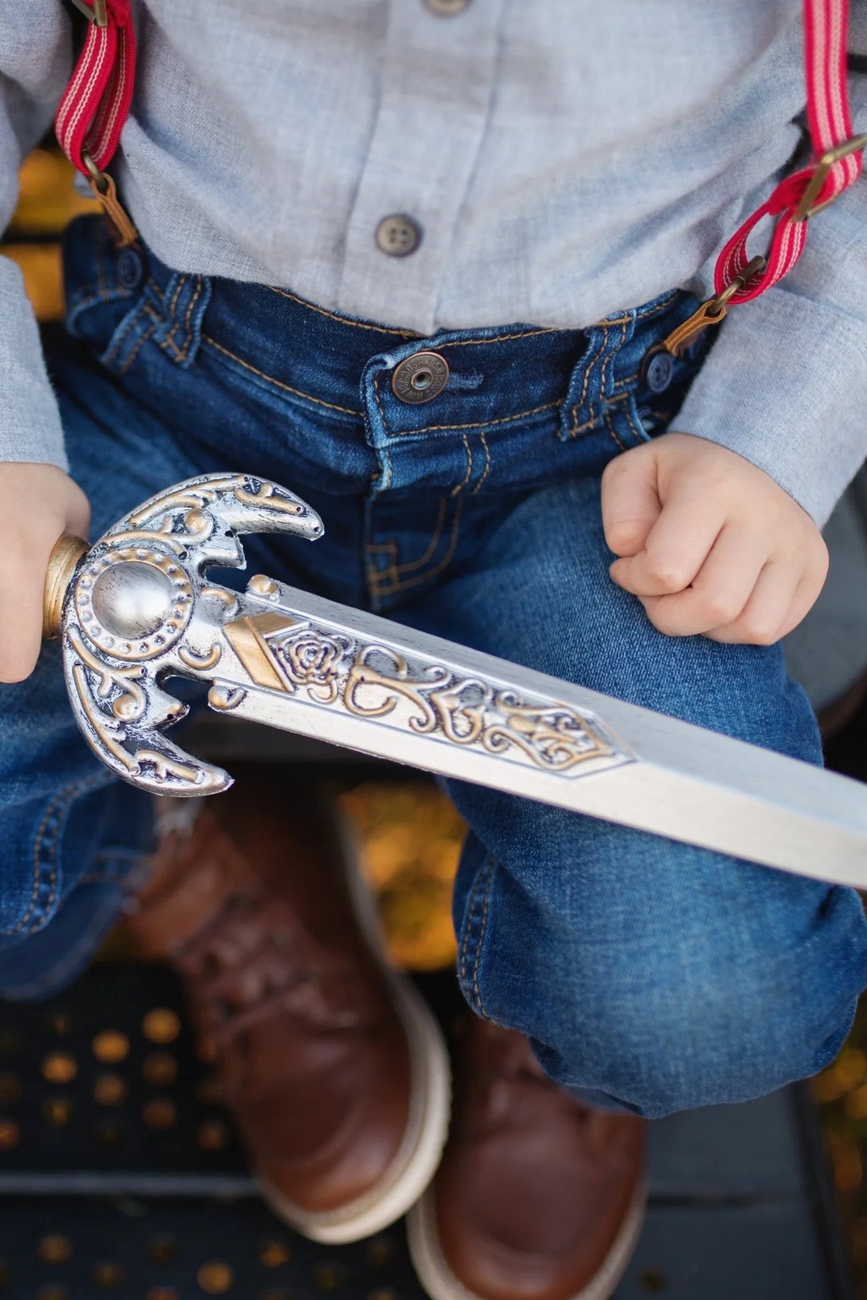 Knight Dagger foam toy with intricate silver and gold details held by child in denim and red suspenders.