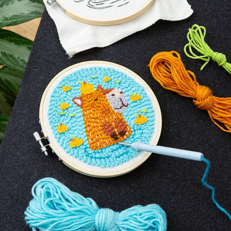 Punch needle embroidery hoop with a cute orange giraffe surrounded by small yellow shapes on blue fabric background