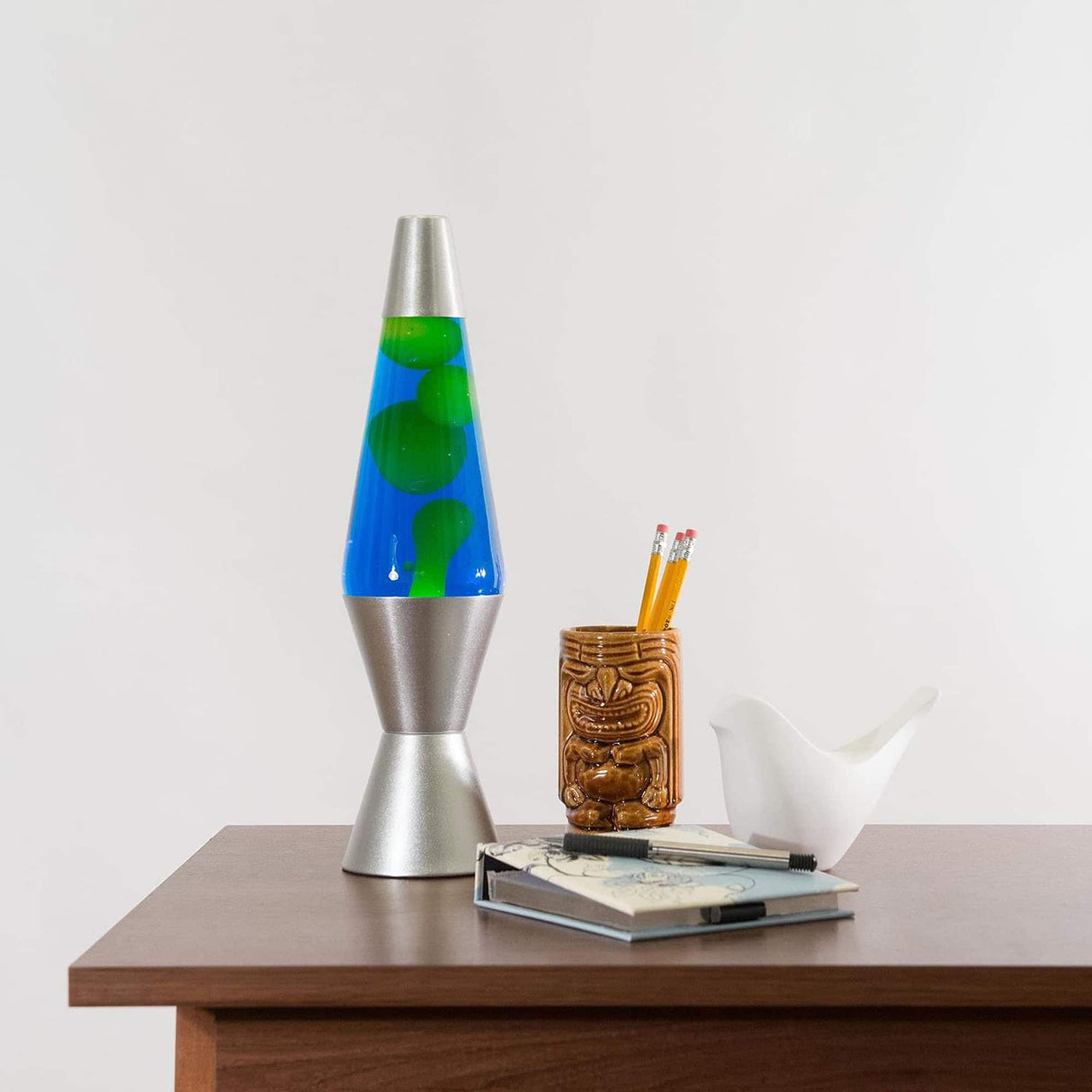 Lava Lamp | Green & Blue featuring slow-moving green wax in blue liquid with silver aluminum base on wooden table.
