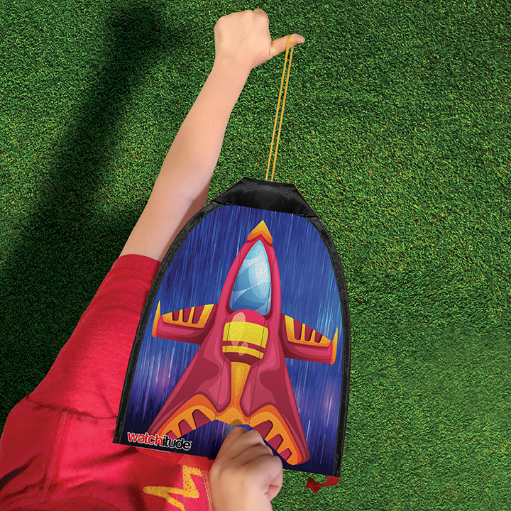 Child holding a vibrant rubber band rocket kite with red and yellow rocket design ready to fly over green grass.
