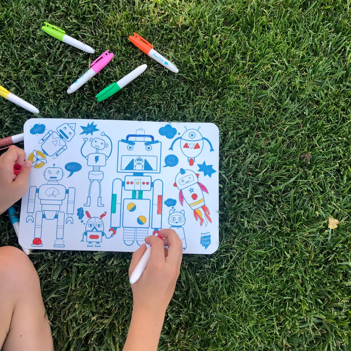 Mini Play Mat Robot showing colorful robot drawings with markers on grass, perfect for kids' creative play outdoors.