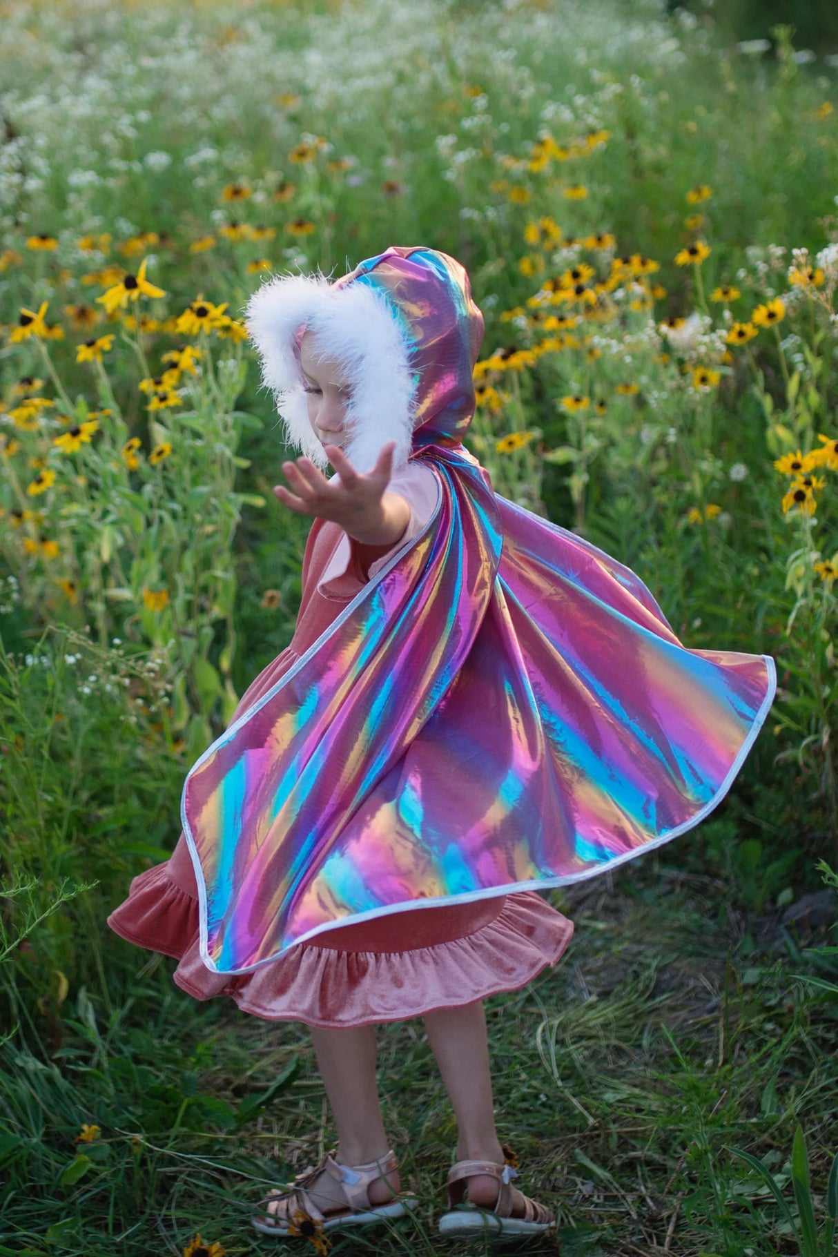 Child spinning outdoors wearing a shimmery Rainbow Princess Cape with fluffy feathery hood trim and sparkly silver edges.