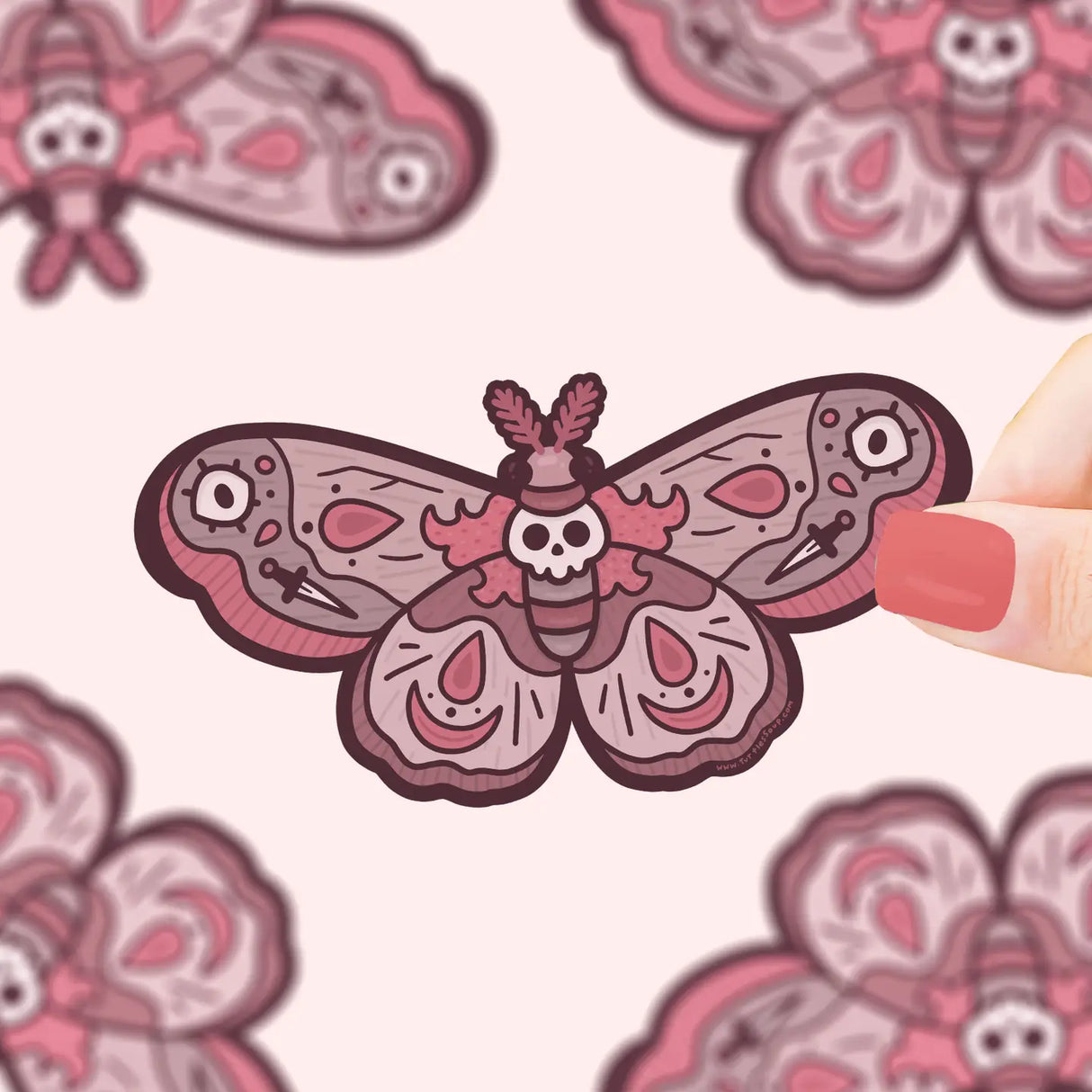 Spooky Skull Moth Sticker showing a detailed vinyl moth with skull design held by fingers on a pale background.