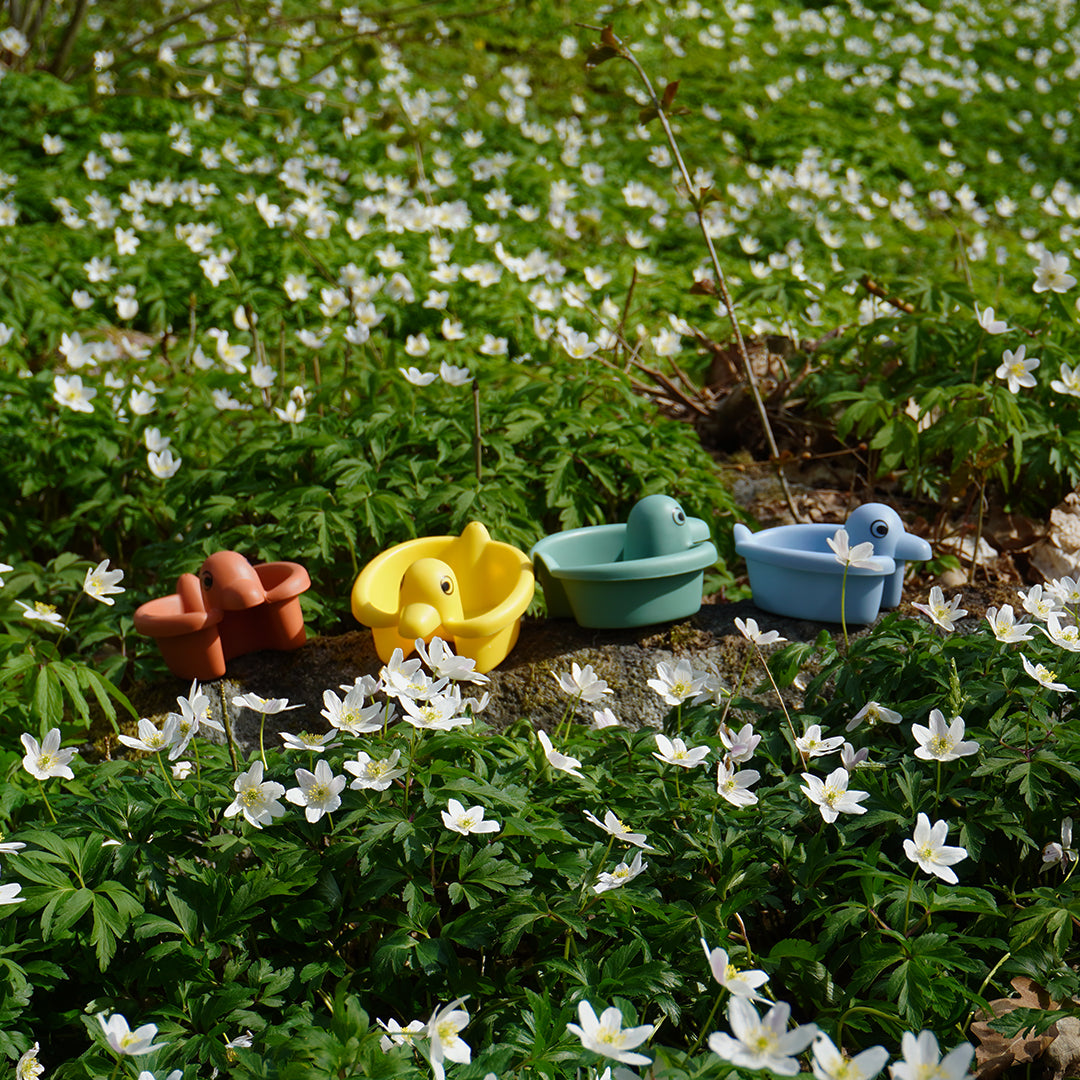 Re:line Bath Ducks set of four colorful duck shaped boats made from 100% recycled plastic in a flower field.