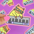 Keyboard Cat Sticker showing a cat wearing glasses playing a keyboard, printed on durable vinyl with a pink border.