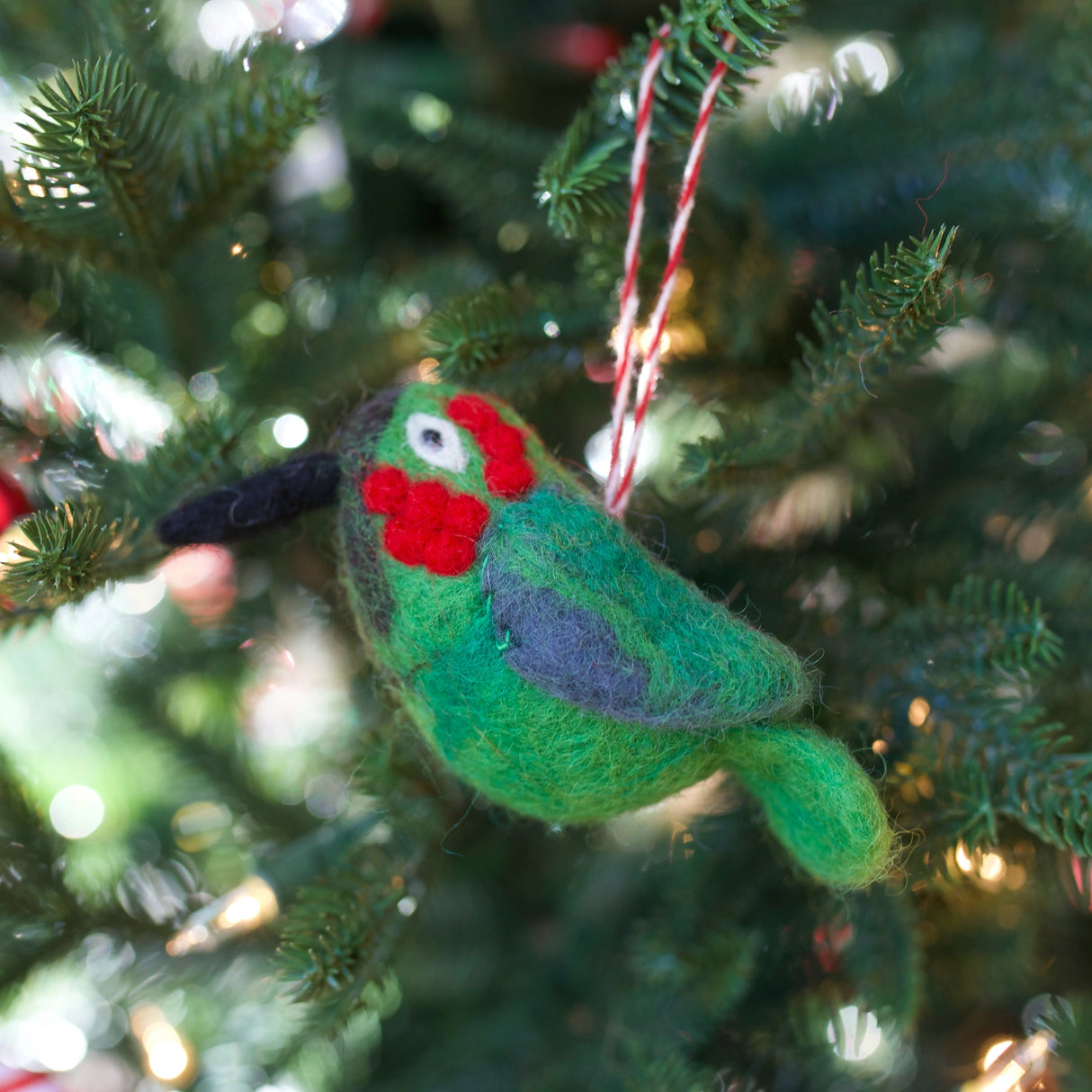 Handmade felt wool bird ornament in green with red and black details hanging on a Christmas tree branch