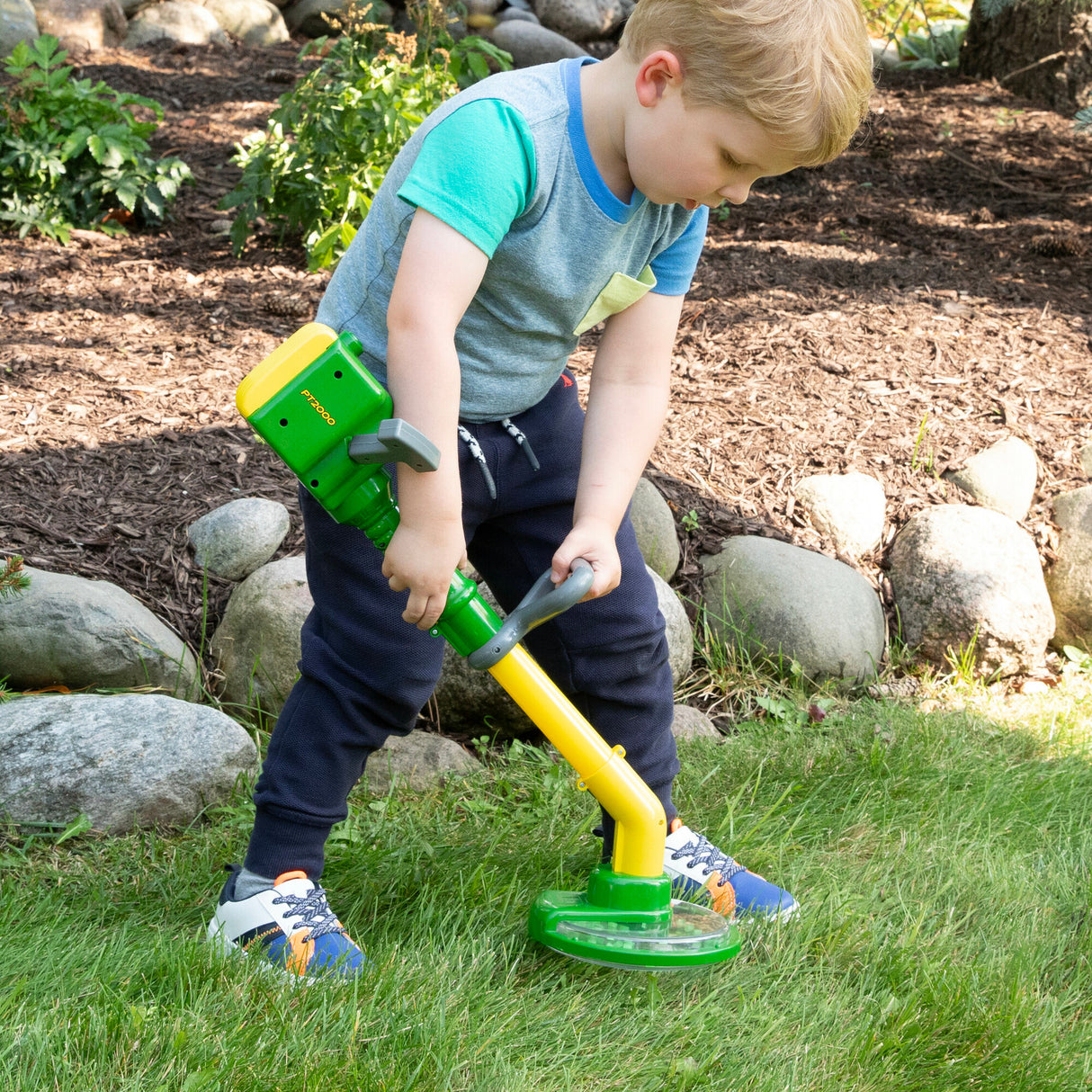 Young boy using the John Deere Weed Trimmer toy outdoors, simulating real weed clipping fun for toddlers.