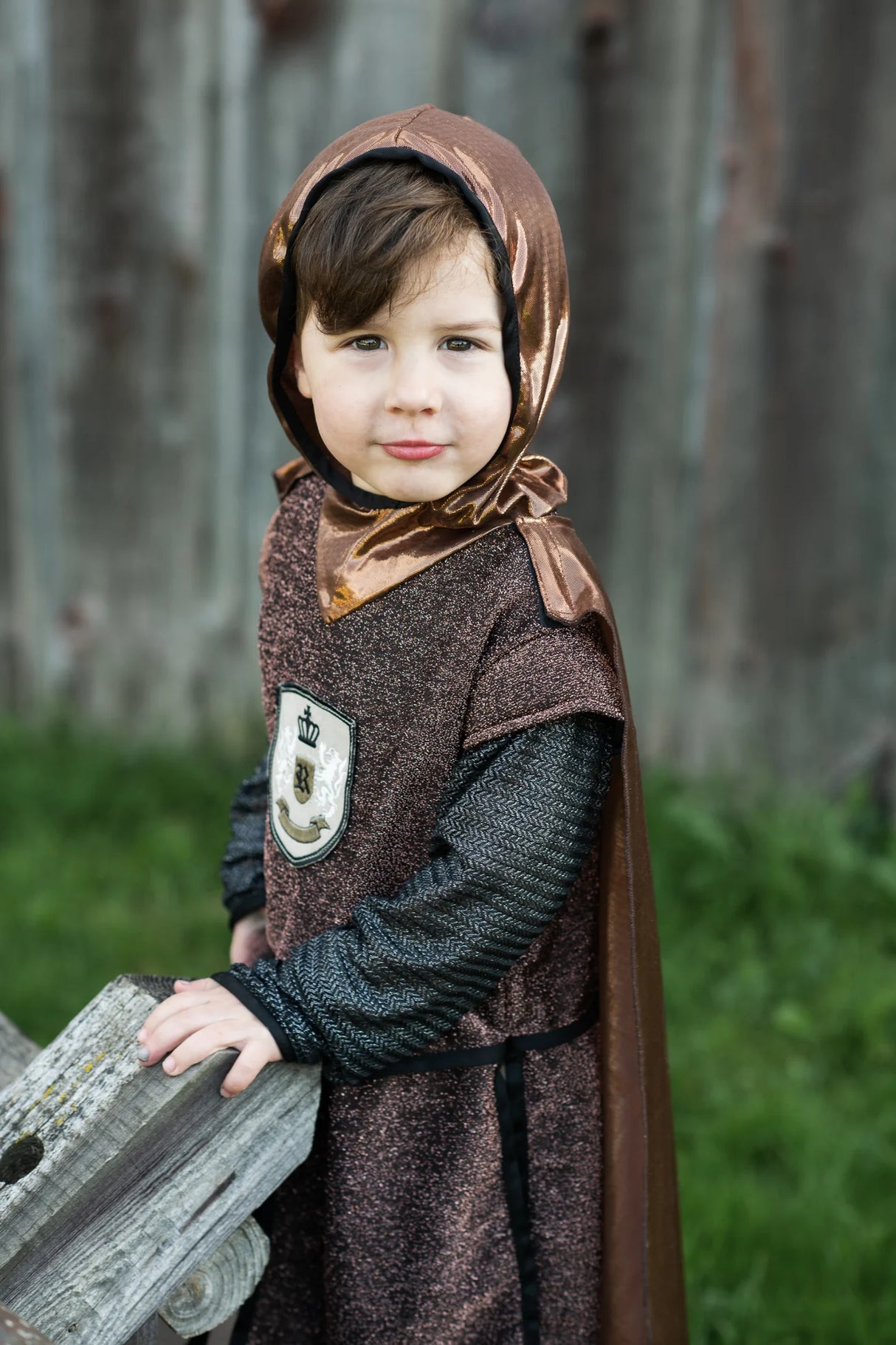 Child wearing the Brilliant Copper Knight Tunic with Cape featuring a sparkly brown tunic, lion emblem, chainmail sleeves, and hooded cape.