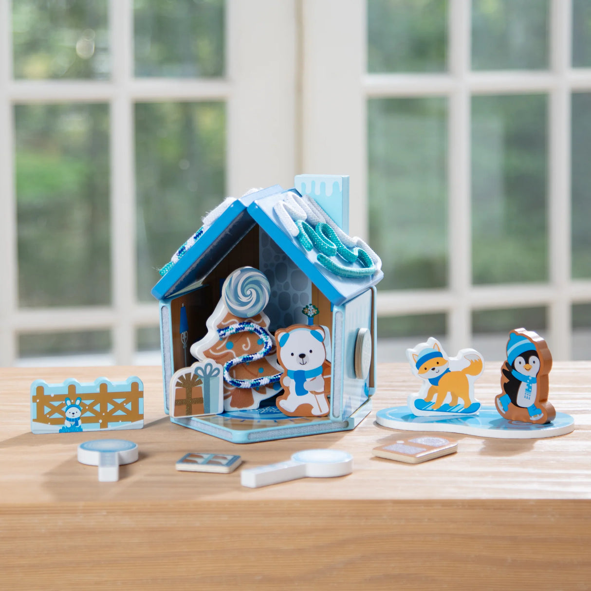 Wooden blue gingerbread house play set with winter animal figures and reusable decorative accessories on wooden table