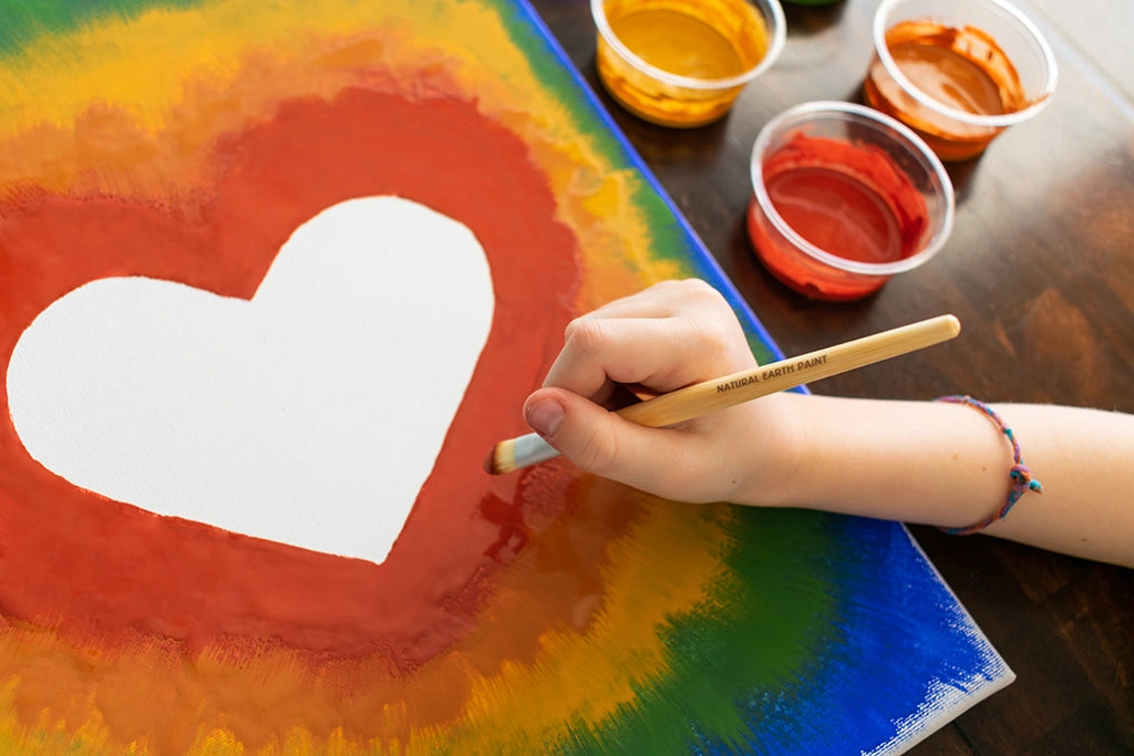 Hand painting a heart on canvas with the Petite Natural Earth Paint Kit using vibrant, natural earth-tone colors.