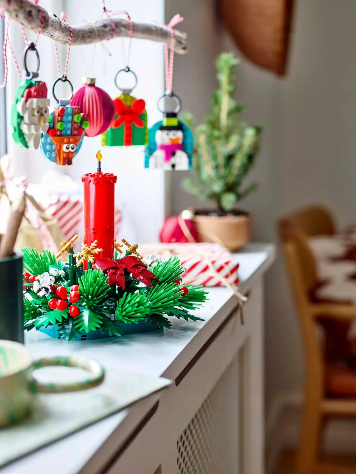 Red candle surrounded by green foliage, red berries, and golden stars Christmas table decoration on a white surface.