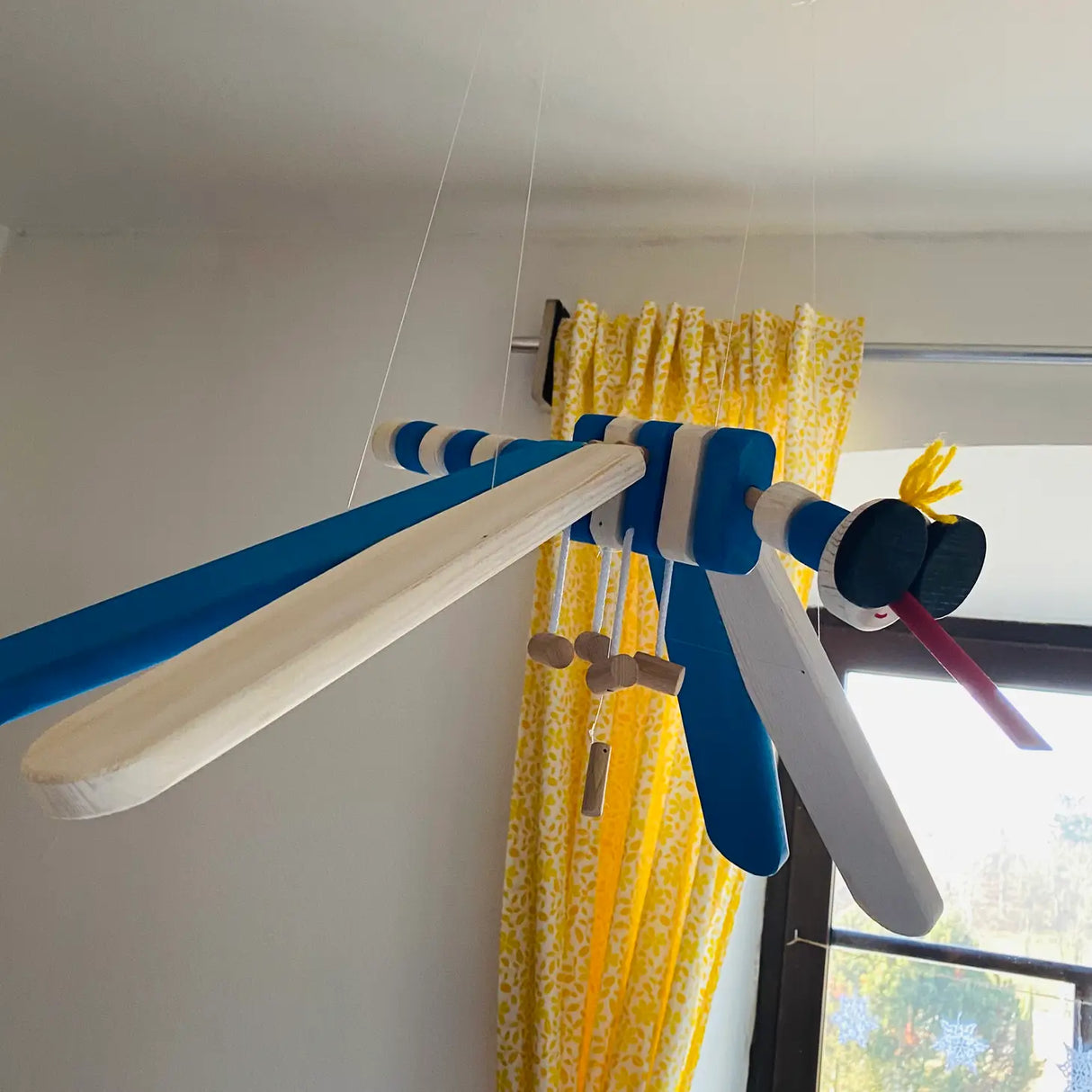 Wooden Mobile Flying Mosquito hanging kinetic wooden mobile with blue and white wings in a bright room.