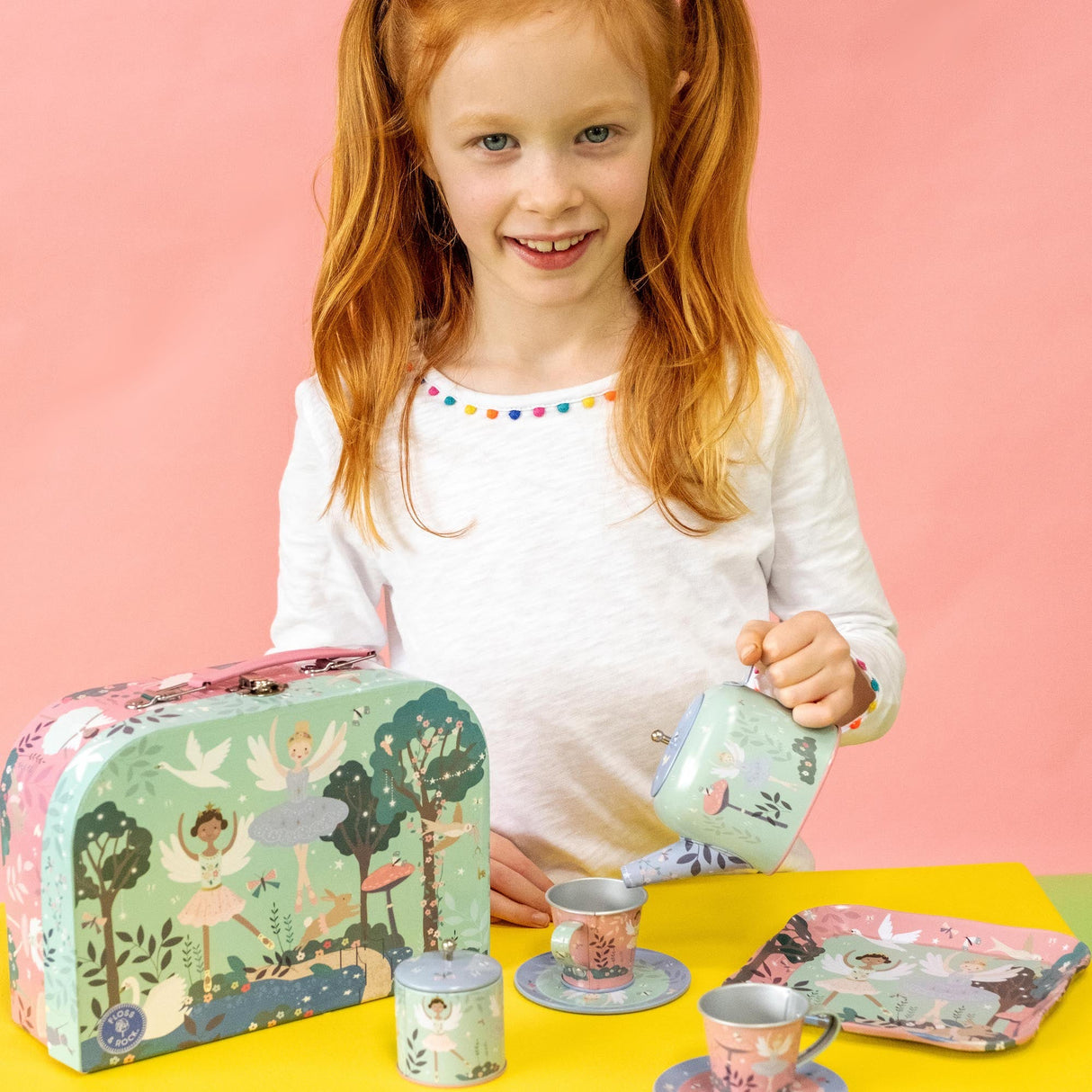 Tea Set | Enchanted showing a girl playing with a pastel, illustrated 9-piece tea set and carry case.