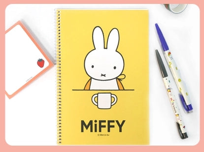 Yellow spiral notebook with a simple white bunny illustration holding a cup and two decorated pens on the side