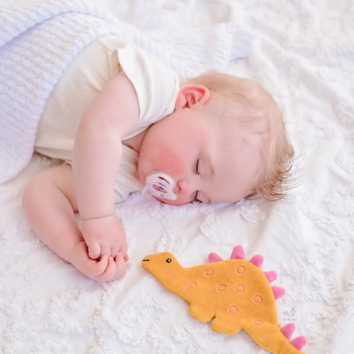 Sleeping baby lying next to Organic Crinkle Fabric | Stego yellow and pink sensory toy on soft white blanket