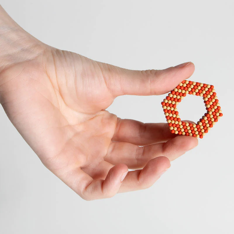 Hand holding a hexagonal shape made of orange and beige Speks Elements Solar magnetic balls desk toy.