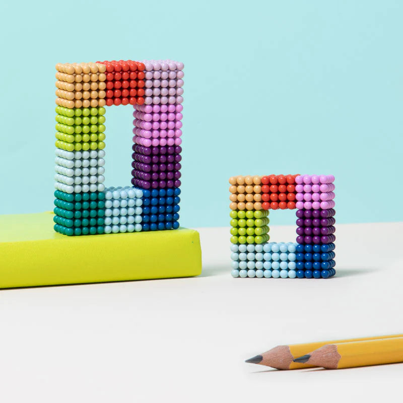 Speks. Matte Spectrum. colorful magnetic balls arranged in square shapes on a light blue background with pencils.