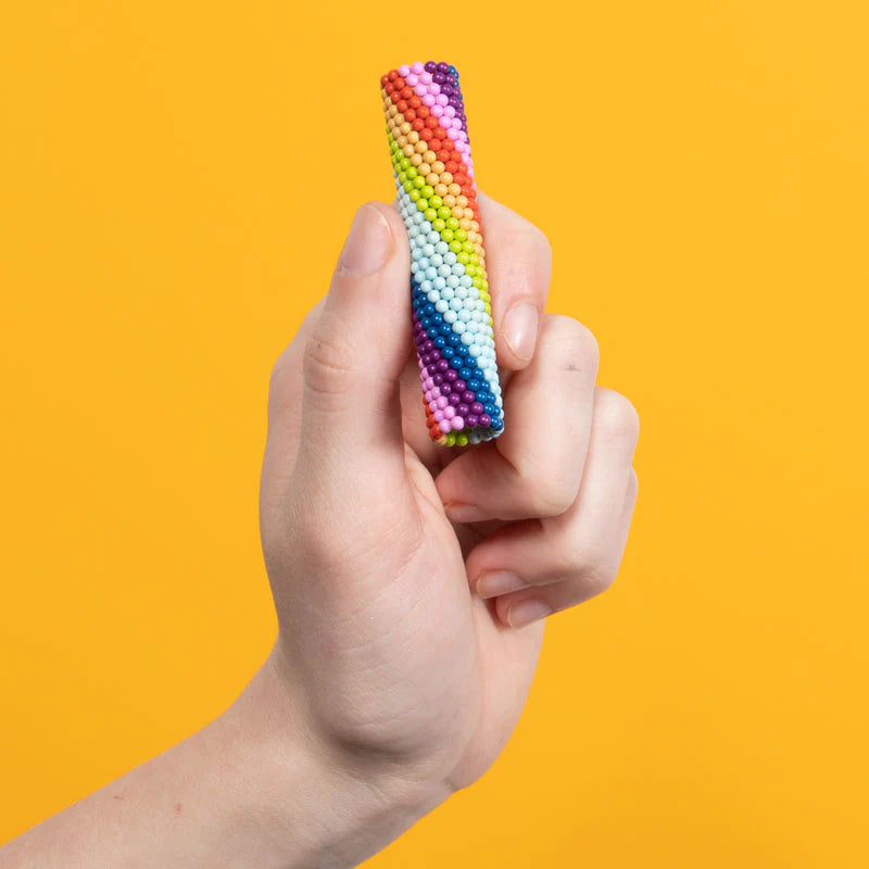 Hand holding colorful Speks. Matte Spectrum magnetic balls in a creative cylindrical shape against yellow background.