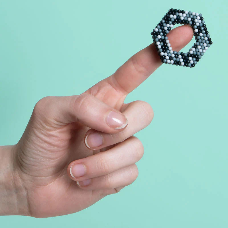 Hand balancing black and white magnetic balls shaped in a hexagon on finger, Speks. Pixel. Game Over. product.