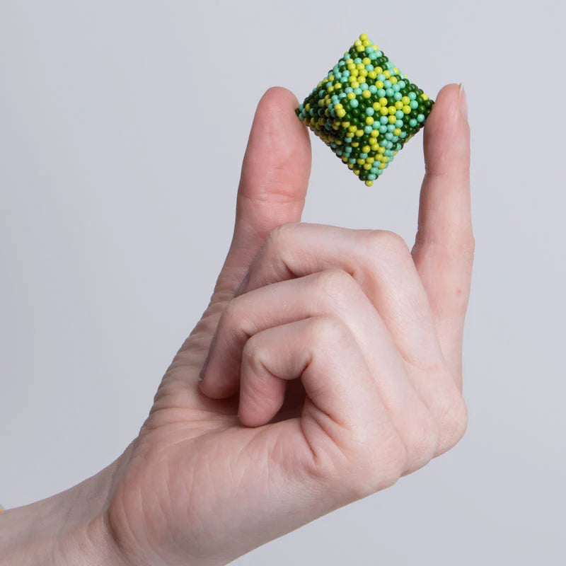 Hand holding a green and yellow cube made of Speks magnetic balls from Speks. Pixel. Motherboard.