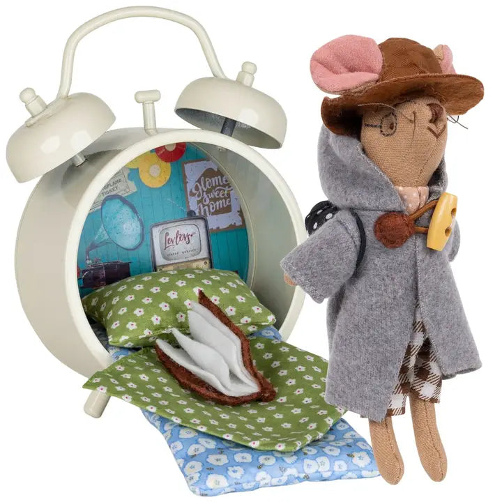 Cute travel mouse doll wearing a grey coat next to a cozy alarm clock bed with floral bedding inside