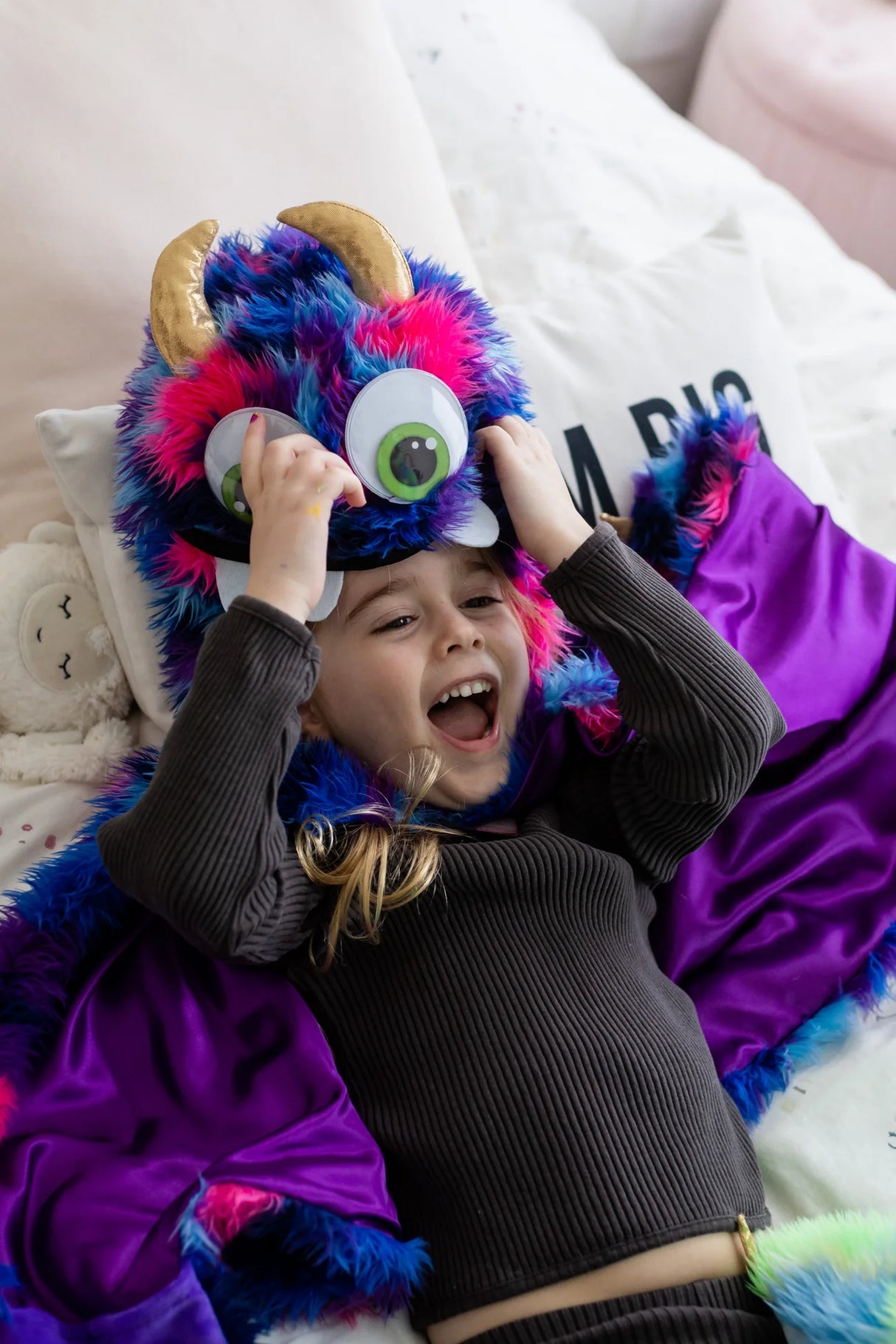 Child wearing colorful Goober the Monster Cape with googly eyes, gold horns, and vibrant blue, pink, and purple fur details.