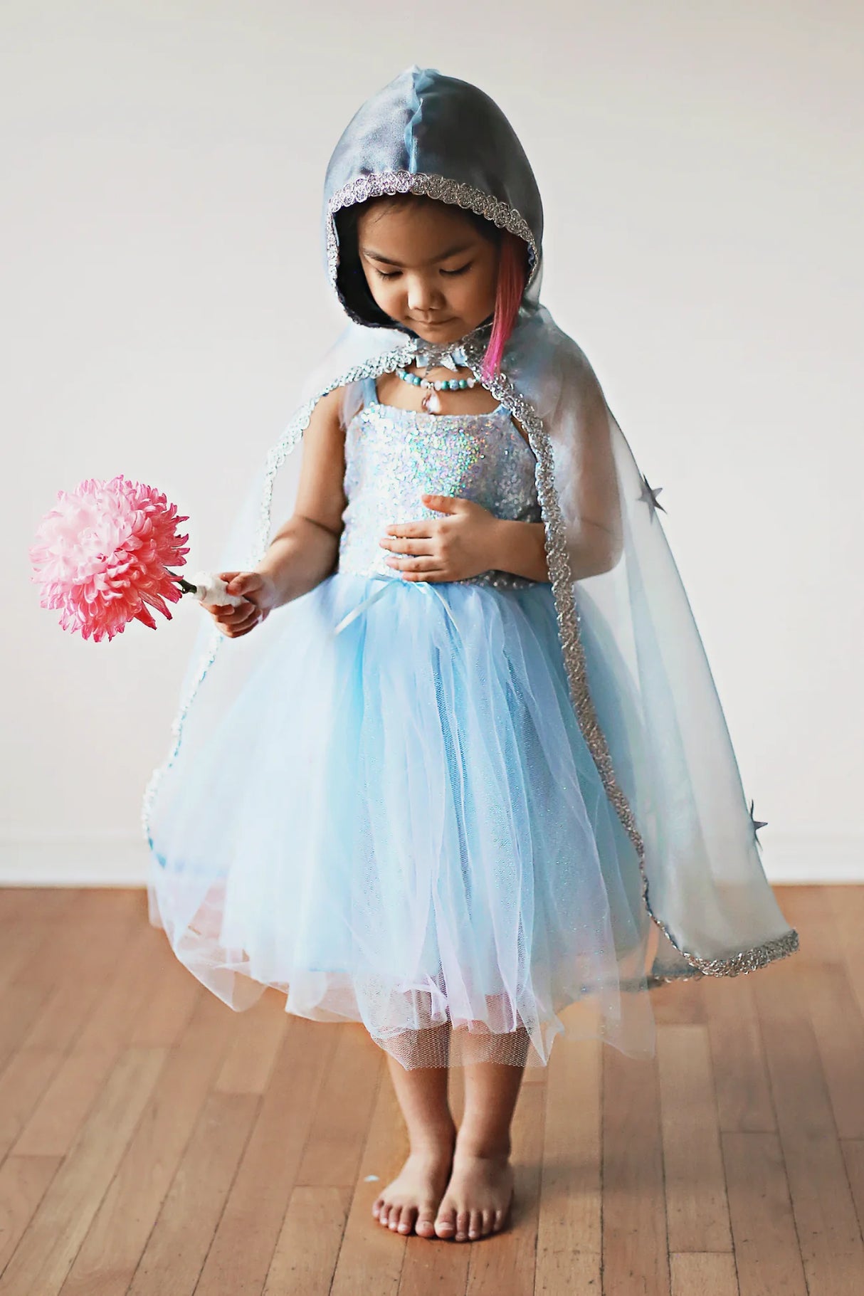 Child wearing Snow Queen Cape | Size 5-6 in blue crystal organza with silver trim and sparkle stars holding a pink flower.