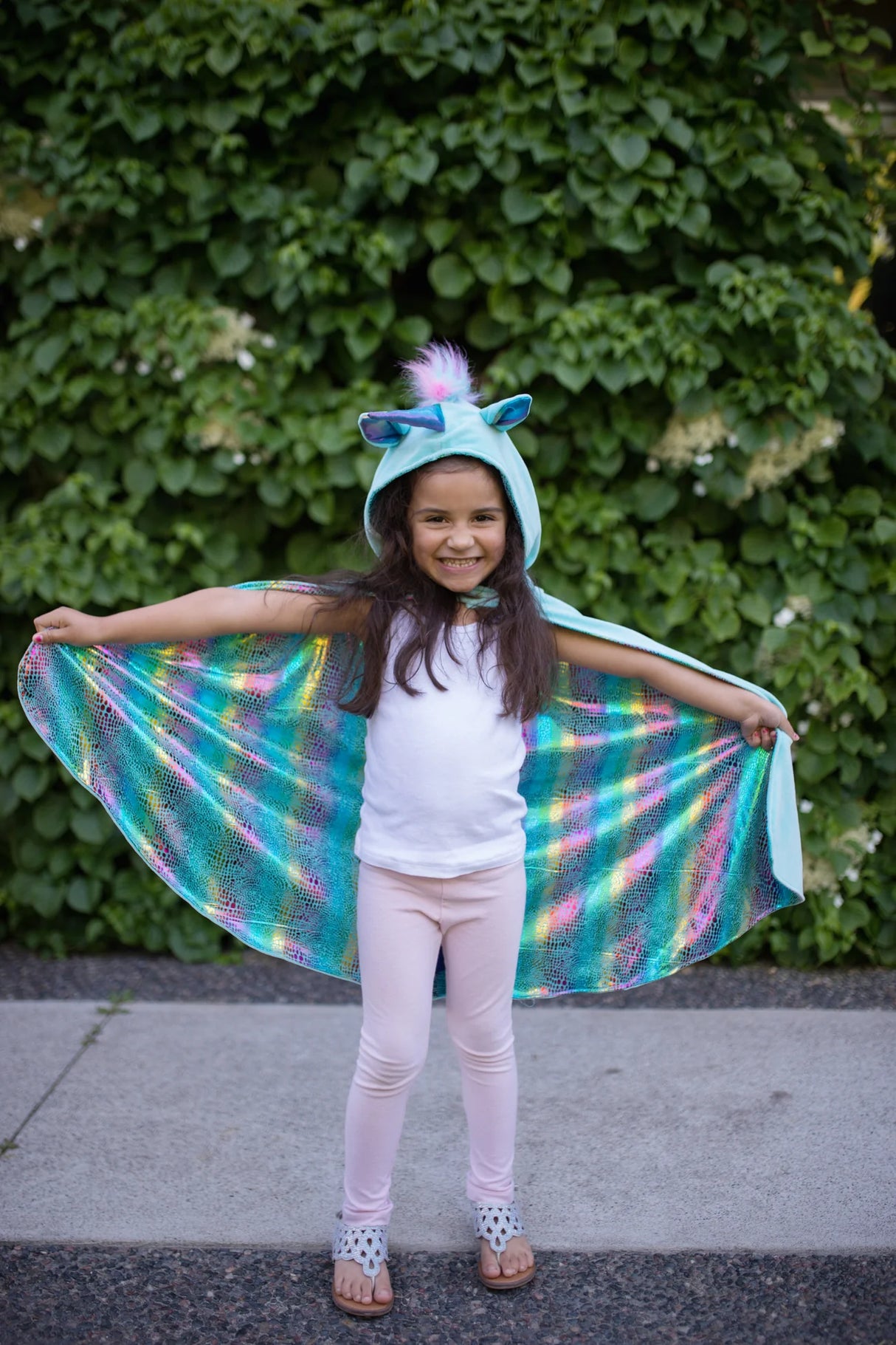 Smiling girl wearing the Unicorn Dragon Reversible Cape showing off the shiny rainbow dragon side outdoors.