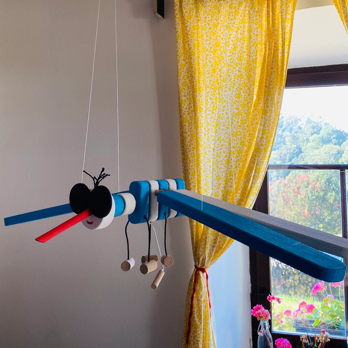 Wooden Mobile Flying Mosquito hanging kinetic wooden mobile in room with yellow curtains and window light background