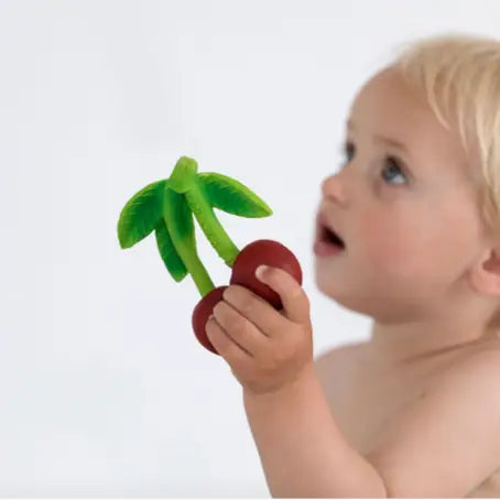 Baby holding a natural rubber cherry-shaped teether with green leaves, safe for soothing gums and sensory play