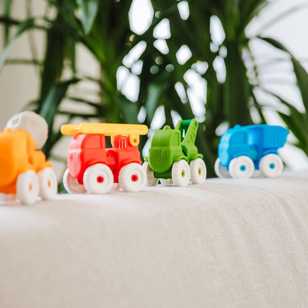 Small plastic toy vehicles in orange, red, green, and blue arranged in a row on a light fabric surface