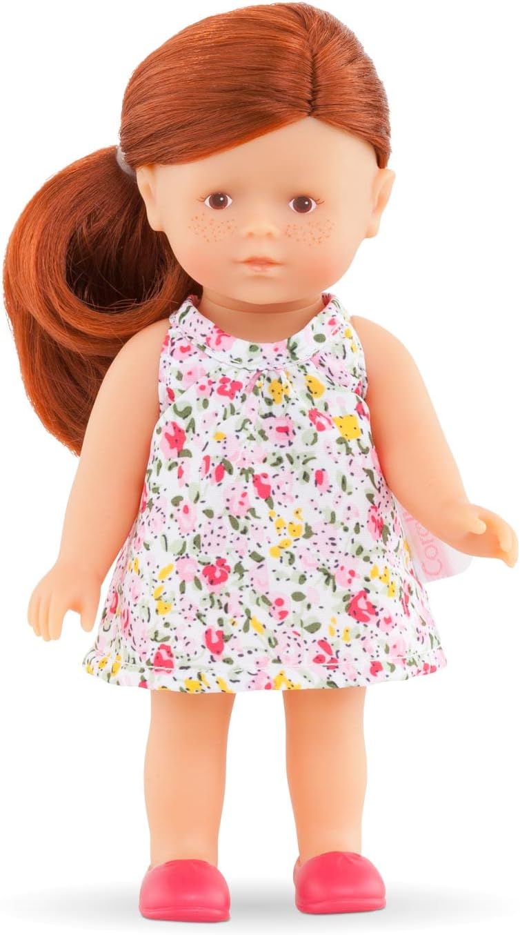 Mini Corolline Ruby doll with red hair, hazel eyes, floral dress, and pink shoes, standing against white background.