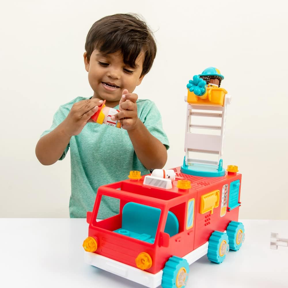Young boy playing with a colorful motorized fire truck toy with a movable ladder and rescue figures on a white table