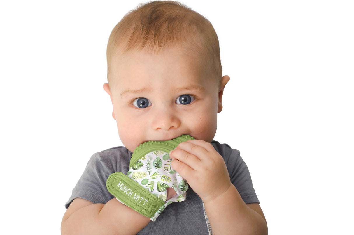 Baby chewing on a green leafy patterned Munch Mitt | Tropical teething mitt with adjustable strap
