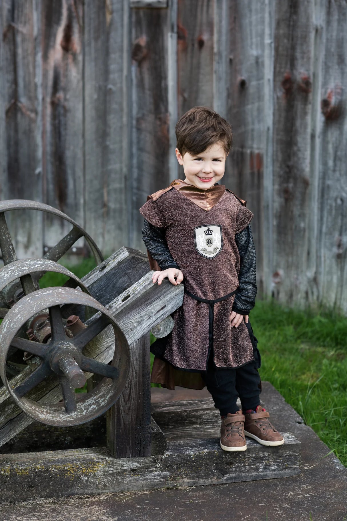 Young boy wearing Brilliant Copper Knight Tunic with Cape in sparkly brown fabric with lion emblem and chainmail sleeves.
